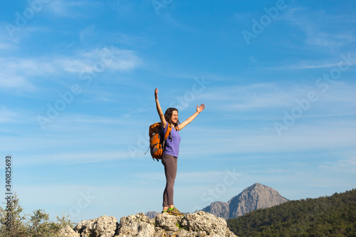 A woman with a backpack stands on top of a mountain and admires the beauty of a mountain valley.