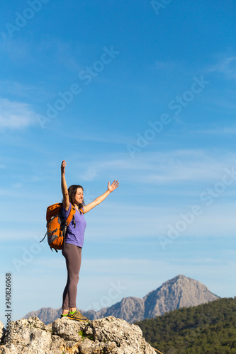 A woman with a backpack stands on top of a mountain and admires the beauty of a mountain valley.