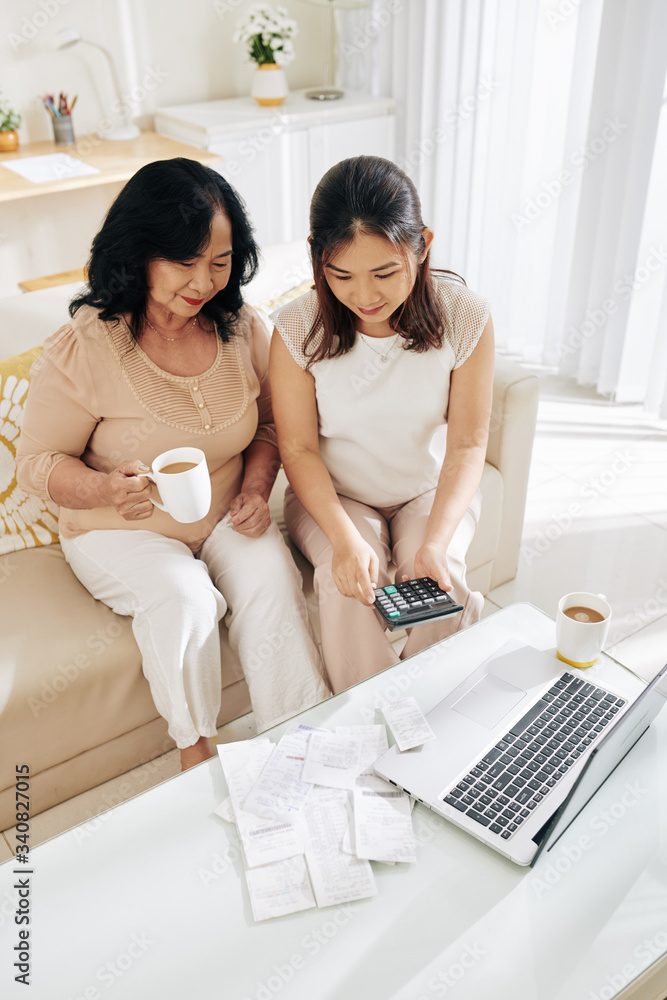 Young Asian woman helping mother with bookkeeping, she is checking bills and paying online Young Asian woman helping mother with bookkeeping, she is checking bills and paying online