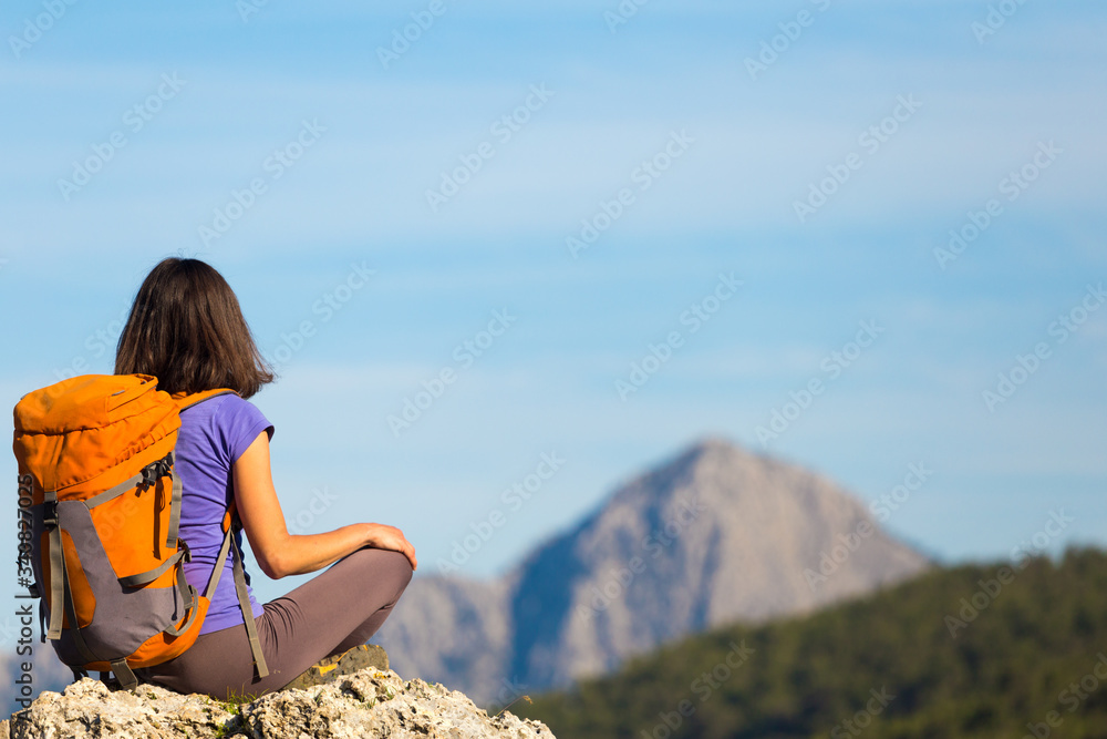 A woman with a backpack sits on top of a mountain and admires the beauty of a mountain valley. A woman with a backpack sits on top of a mountain and admires the beauty of a mountain valley.