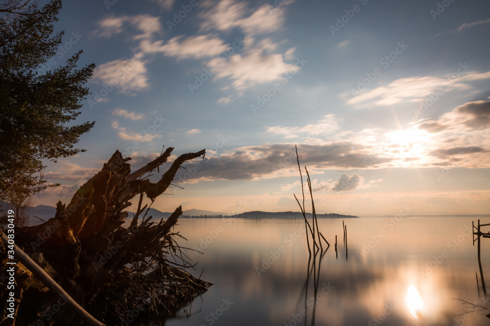 Sunset at Trasimeno lake (Umbria, Italy), with fishing net poles and trees on perfectly still water Sunset at Trasimeno lake (Umbria, Italy), with fishing net poles and trees on perfectly still water