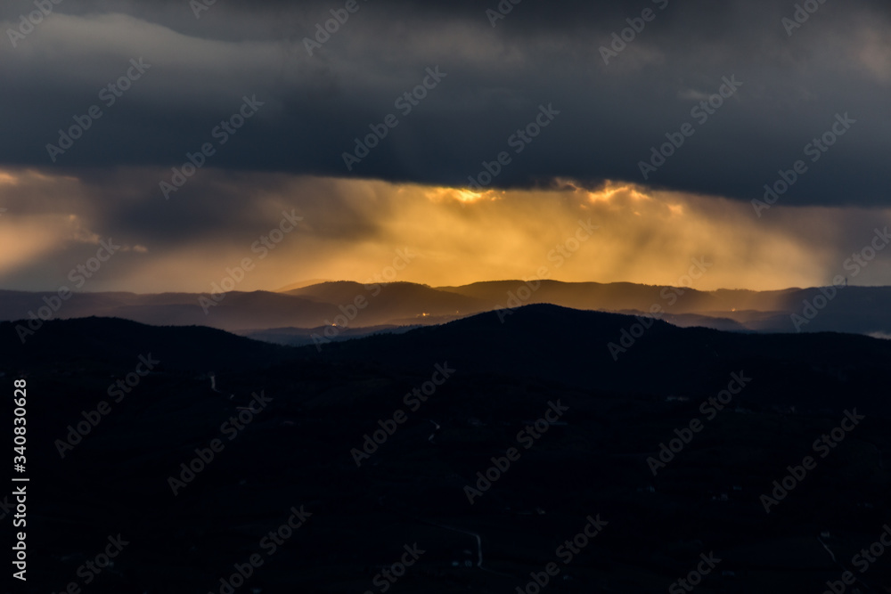 Obraz premium Sunrays coming over mountains beneath moody clouds