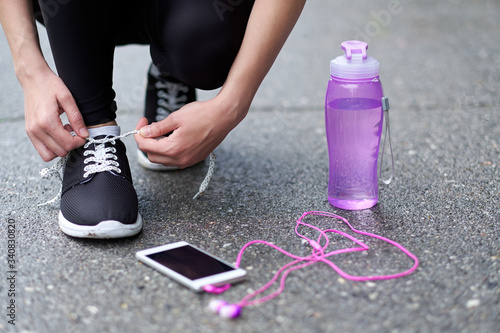 runner woman tying running shoes laces getting ready for race on run track stadium with bottle of water and phone with headphones