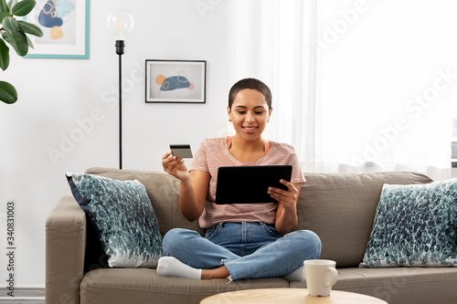 internet banking, online shopping and technology concept - happy smiling african american woman sitting on sofa with tablet pc computer and credit card at home