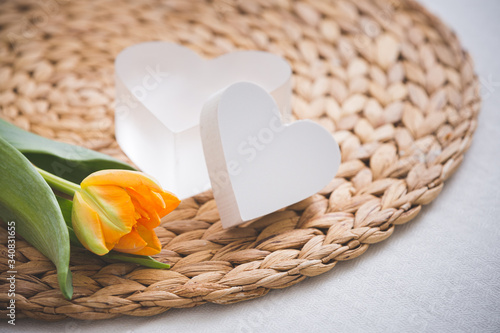 Closeup of an orange tulip and two hearts on wicker straw background. Spring mood