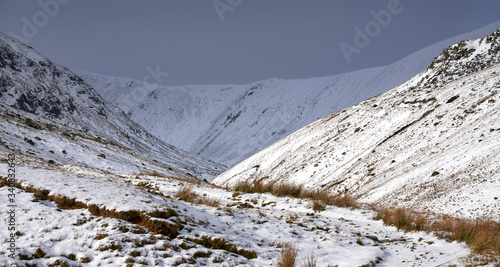 Snow and ice covered mountain ridges illuminated by the sun in the Lake District on a cold winters day. In the distance is Lower Man, Kepple Cove and Catstye Cam on the left. photo