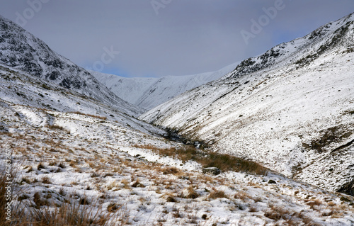 Snow and ice covered mountain ridges illuminated by the sun in the Lake District on a cold winters day. In the distance is Lower Man, Kepple Cove and Catstye Cam on the left. photo