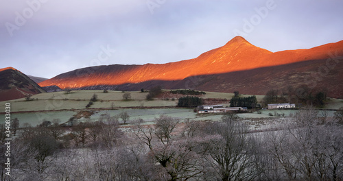 A frost covered valley of Newlands with a winters sunrise catching the mountain top of Causey Pike, Derwent Fells in the Lake District. photo