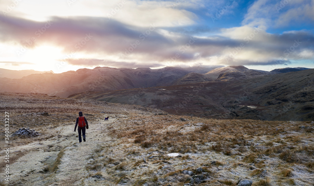 A hiker an their dog descending High Spy on the mountain trail that leads to the summit of Dale Head on a cold winters sunrise in the Lake District.