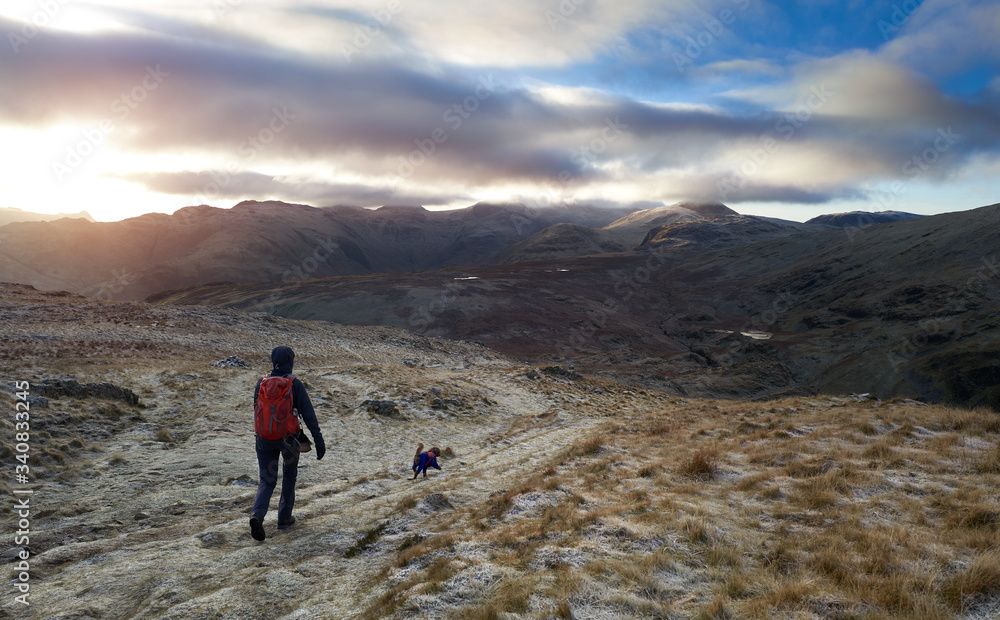 A hiker an their dog descending High Spy on the mountain trail that leads to the summit of Dale Head on a cold winters sunrise in the Lake District.
