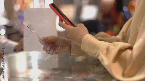 An upwardly mobile Asian Muslim woman using a mobile phone - smartwatch to pay for a product at a sale terminal with nfc identification payment for verification and authentication