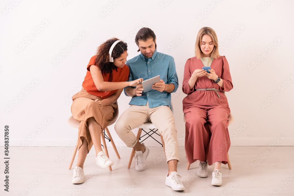 Obraz premium Brown-haired man sharing information on internet with Afro-American woman in wireless headphones while blonde girl texting sms