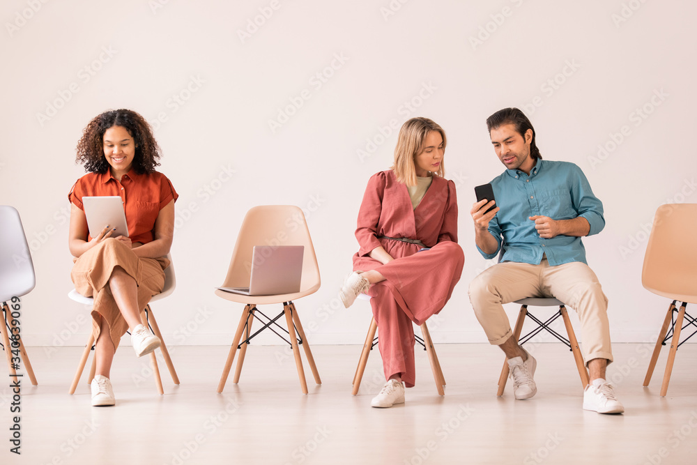 Obraz premium Modern young man showing new convenient smartphone app to girl while black woman talking via video chat on tablet