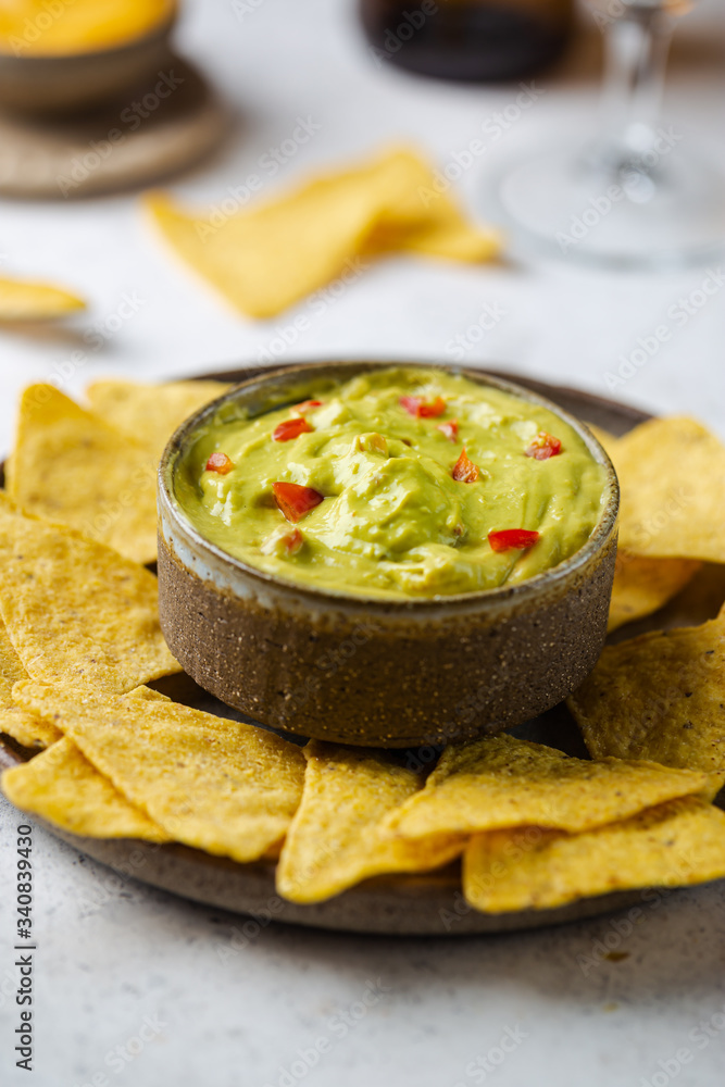 Nachos chips in a bowl with sauces guacamole and beer over white stone background.