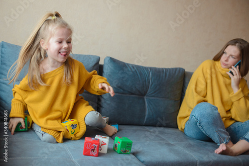 stay at home. Mom and daughter in yellow sweaters on a gray sofa spend time together at home in quarantine
