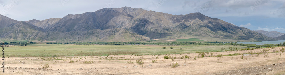 flat fields and barren slopes near Benmore lake in green valley, New Zealand flat fields and barren slopes near Benmore lake in green valley, New Zealand