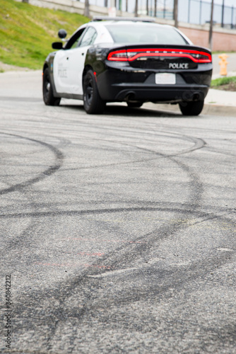 Tire marks in the road from cars doing donuts. with a blurred police car in the background. 