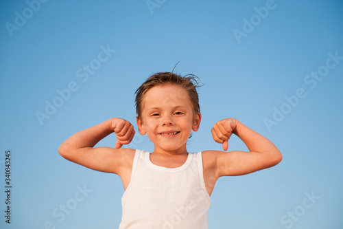 happy healthy little athlete kid in white tank top on blue sky background