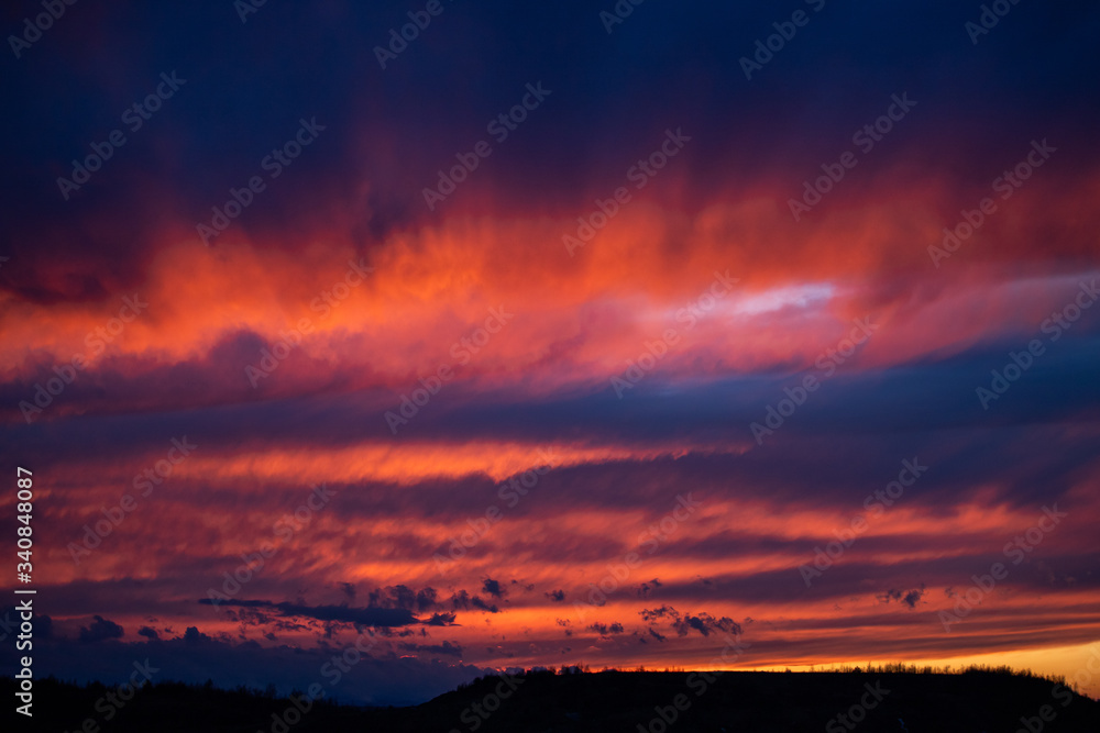 Bright red sunset among blue clouds. Mystical silhouettes in clouds