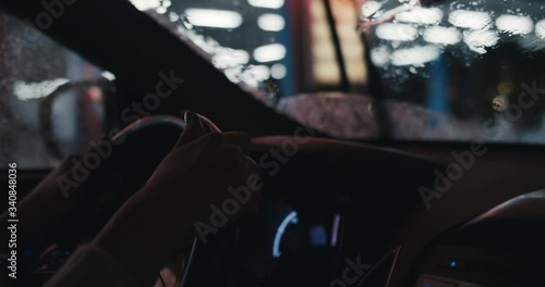 Woman driving a car by an empty garage traveling on a regional road trip staycation rainy night after pandemic tourism steering wheel close up