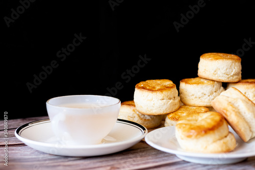 a white cup of tea and Traditional British Scones on wooden table black background, breakfast food teatime .