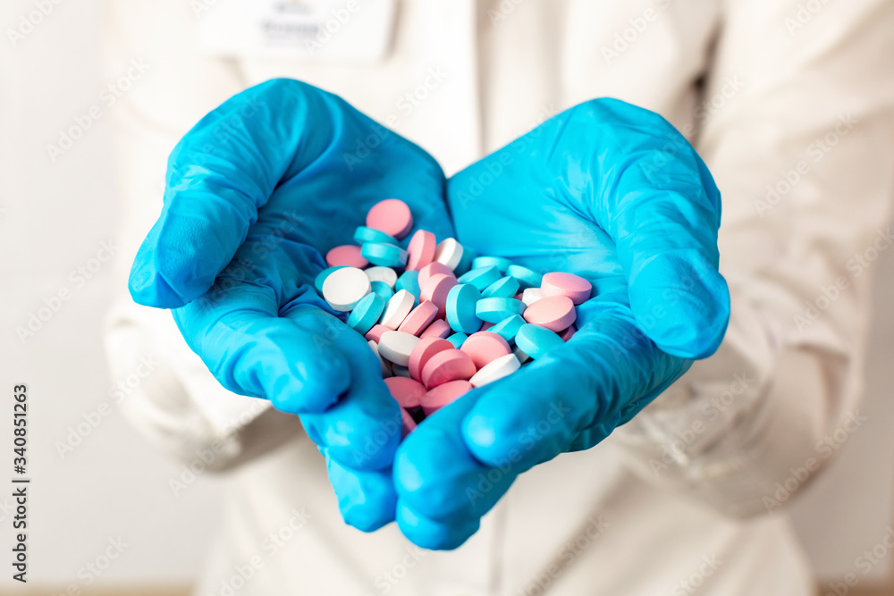 Close-up the doctors hands in the shape of a heart in blue medical gloves are stretched forward and hold multi-colored pills. Medicine, vitamins and antibiotics for the treatment of health. Close-up the doctors hands in the shape of a heart in blue medical gloves are stretched forward and hold multi-colored pills. Medicine, vitamins and antibiotics for the treatment of health.