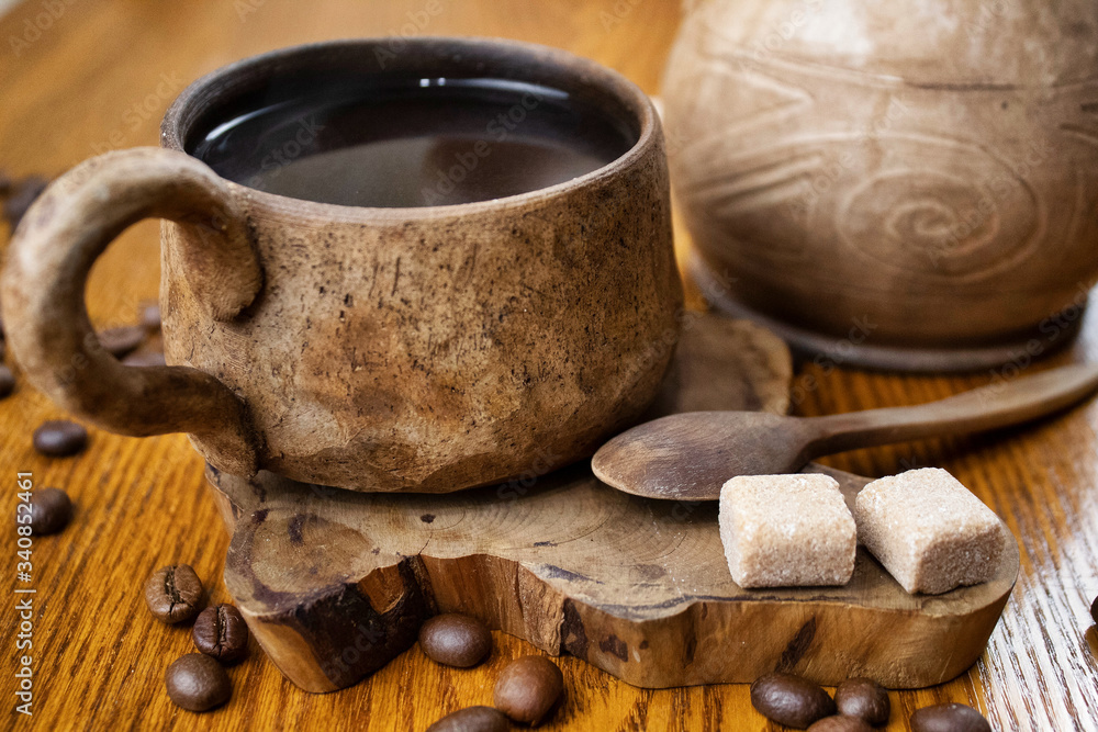 Ceramic coffee set in folk style close up. Juniper cup holder and coffee spoon. Fragrant coffee beans and brown sugar cubes. Coffee beans are scattered on a wooden table. Composition in warm colors. Ceramic coffee set in folk style close up. Juniper cup holder and coffee spoon. Fragrant coffee beans and brown sugar cubes. Coffee beans are scattered on a wooden table. Composition in warm colors.