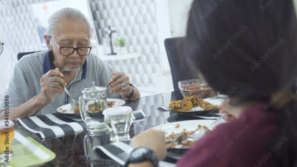Elderly man having lunch with his granddaughter while sitting together in the dining table at home. Shot in 4k resolution Elderly man having lunch with his granddaughter while sitting together in the dining table at home. Shot in 4k resolution