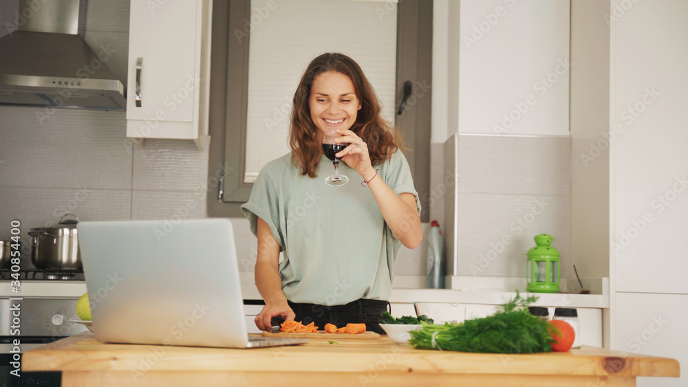 Young beautiful girl woman cooks in the kitchen online with a glass of wine in her hands, cooking classes, chatting with friends, parties online Young beautiful girl woman cooks in the kitchen online with a glass of wine in her hands, cooking classes, chatting with friends, parties online