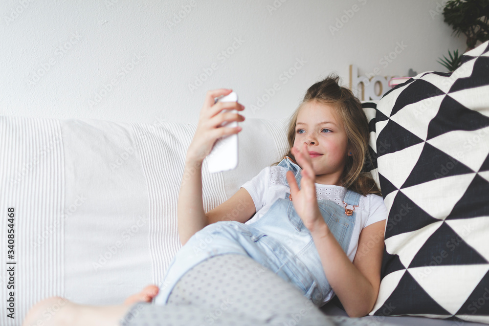 young beautiful girl with smartphone on couch is doing video call during the corona crisis young beautiful girl with smartphone on couch is doing video call during the corona crisis