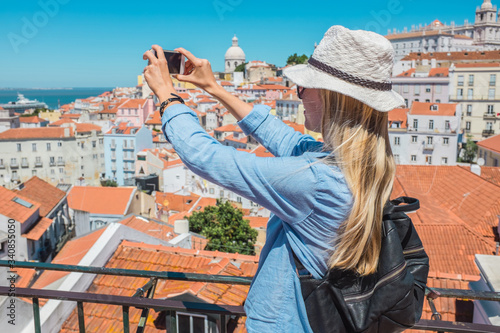 Young traveler woman with smartphone takes pictures in Lisbon of city under sky summer 