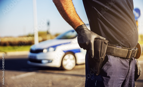 Fototapeta Naklejka Na Ścianę i Meble -  Police officer pulling a gun on the street, in background police car.
