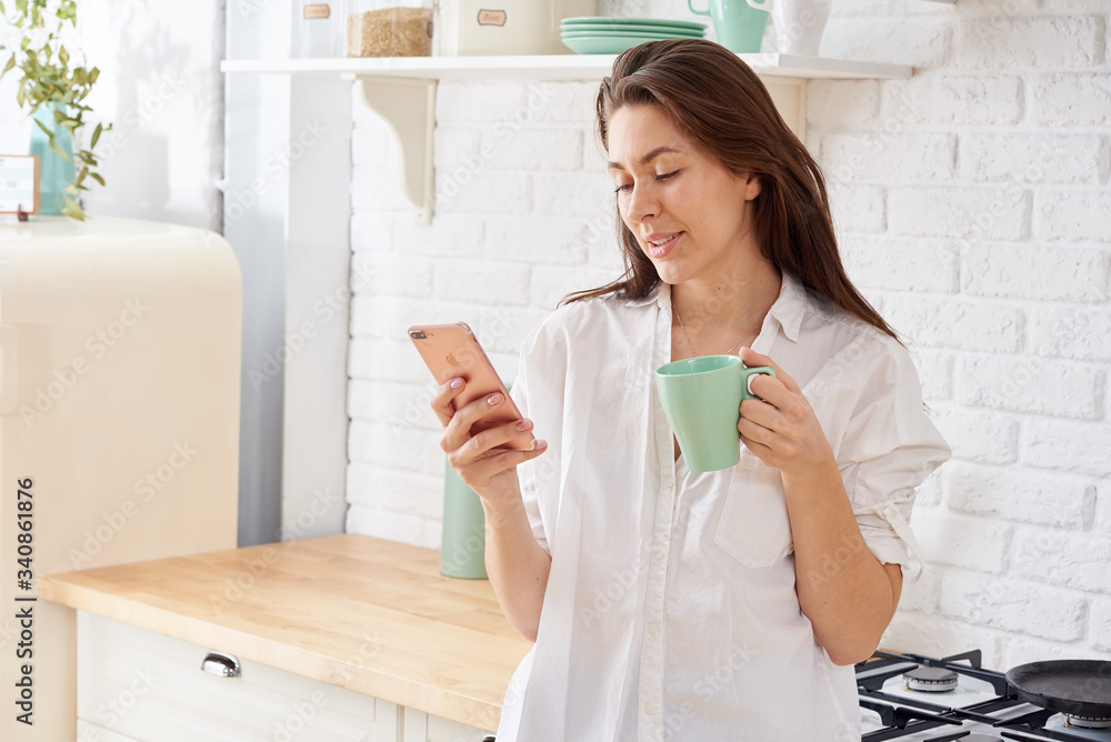 Young beautiful woman using cell phone and having a coffee in the kitchen Young beautiful woman using cell phone and having a coffee in the kitchen