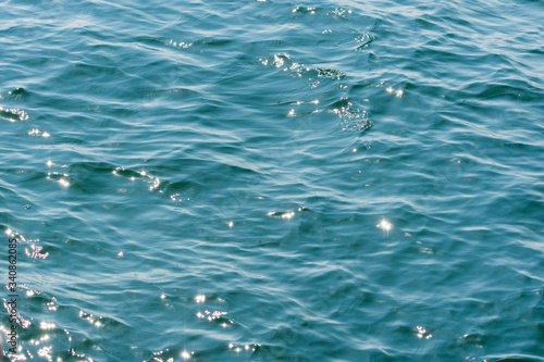 Close-up smooth blue ocean wave with sun reflection. Beautiful natural wallpaper.