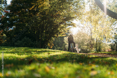 19/4/2020 Asian woman with a bike feeding a dog in autumn at the Botanic garden, Oamaru, New Zealand. Concept about exercise while social isolation from Coronavirus or Covid 19.
