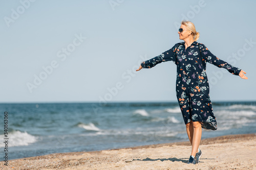 End of quarantine. Young blonde woman in sunglasses and long dress walking on beach