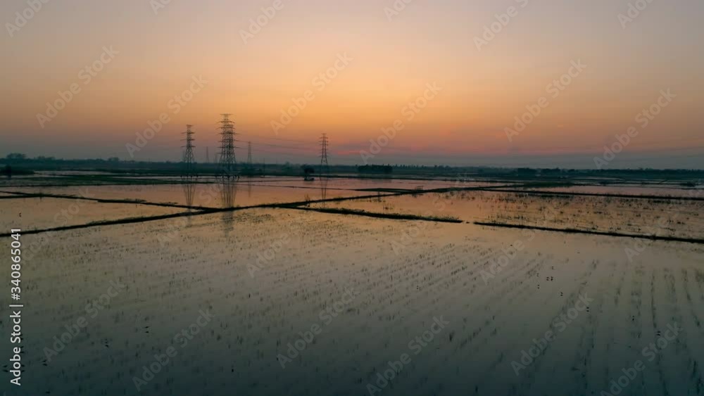 Drone video shot.Aerial view flooded rice agricultural rural fields with electric line pylon.  sunset sunrise in summer or spring season with pretty clouds.