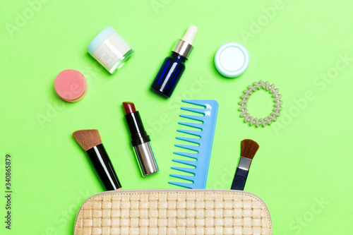 Top view od cosmetics bag with spilled out make up products on green background. Beauty concept with empty space for your design