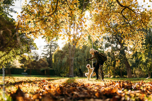 19/4/2020 Asian woman with a bike feeding a dog in autumn at the Botanic garden, Oamaru, New Zealand. Concept about exercise while social isolation from Coronavirus or Covid 19.