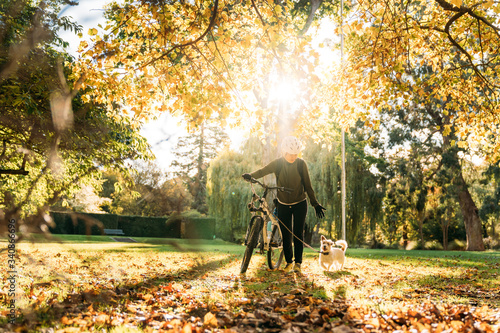 19/4/2020 Asian woman with a bike walking with a dog in autumn at the Botanic garden, Oamaru, New Zealand. Concept about exercise while social isolation from Coronavirus or Covid 19.