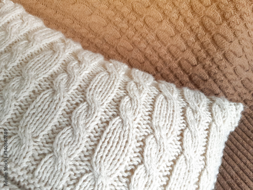 Handmade knitted pillow on brown plaid with cables knit stitches design. Cosy home decor wallpaper, soft blur, light flash effect texture Handmade knitted pillow on brown plaid with cables knit stitches design. Cosy home decor wallpaper, soft blur, light flash effect texture