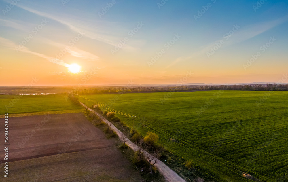 Aerial view of agriculture land at Palava hills, Czech republic. Rural scene near vineyards with power line above dirty road. Summer weather, sunset time. Nove mlyny water lake in background.
