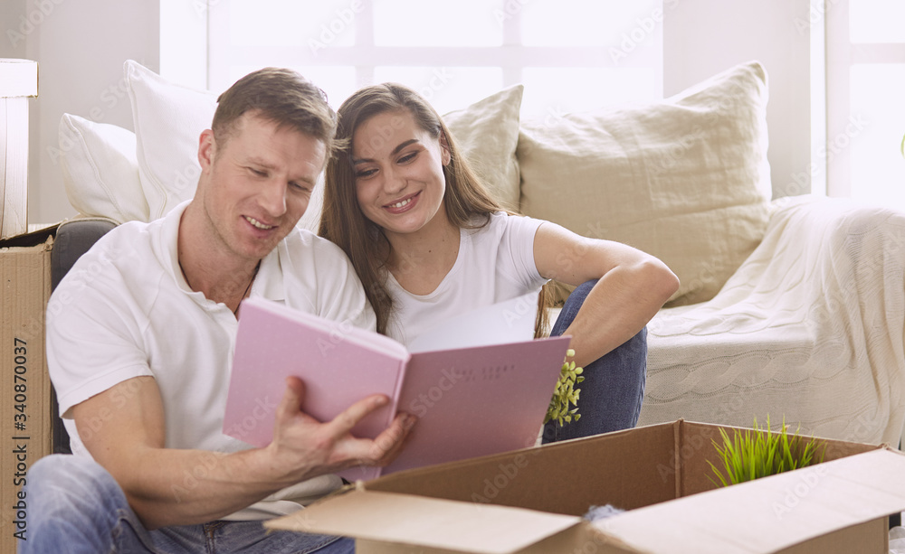 Portrait of happy couple looking at laptop computer together sitting in new house, surrounded with boxes Portrait of happy couple looking at laptop computer together sitting in new house, surrounded with boxes