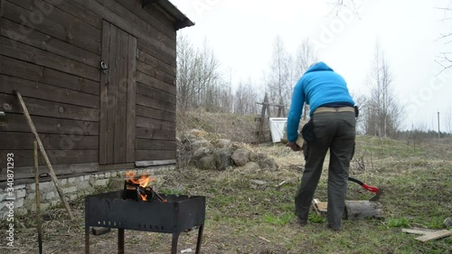 Man brings firewood from birch and kindles a fire in a brazier. 