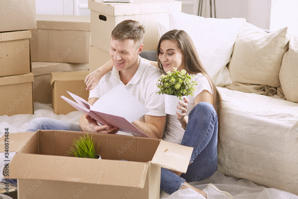 Portrait of happy couple looking at laptop computer together sitting in new house, surrounded with boxes Portrait of happy couple looking at laptop computer together sitting in new house, surrounded with boxes