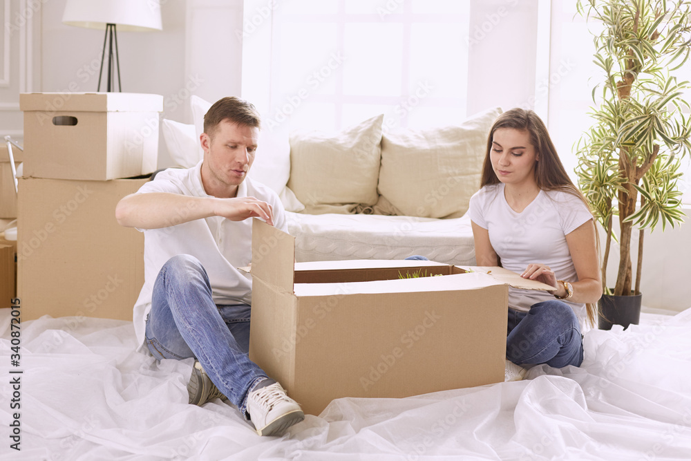 Portrait of happy couple looking at laptop computer together sitting in new house, surrounded with boxes Portrait of happy couple looking at laptop computer together sitting in new house, surrounded with boxes