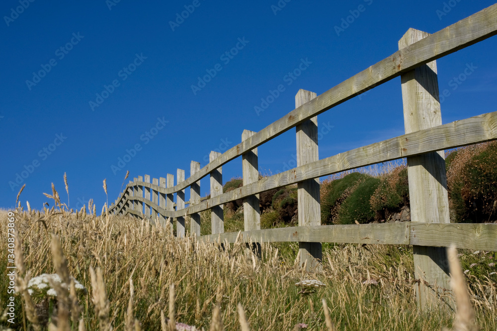 A wooden fence along a field with clear blue sky