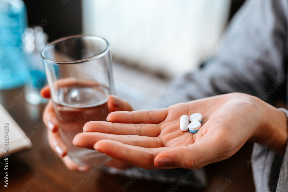 Businesswomen working at home with glass of water takes white round pill in hand. Businesswomen working at home with glass of water takes white round pill in hand.