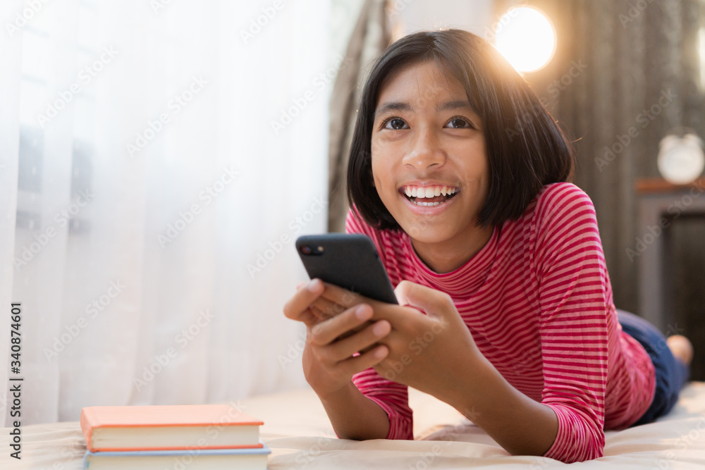 Happy Asian girl using the smartphone while lying in the bedroom at home night, Asia child smile and enjoy the laugh expression on the face. Concept relax and lifestyle at home Happy Asian girl using the smartphone while lying in the bedroom at home night, Asia child smile and enjoy the laugh expression on the face. Concept relax and lifestyle at home