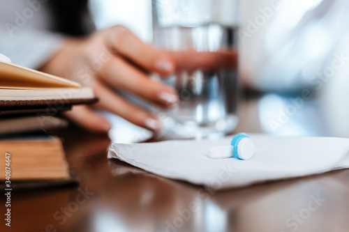 white round pill on tissue and blur hand take a glass of water.